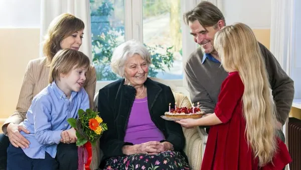 Дети преподносят подарки бабушке — торт и цветы