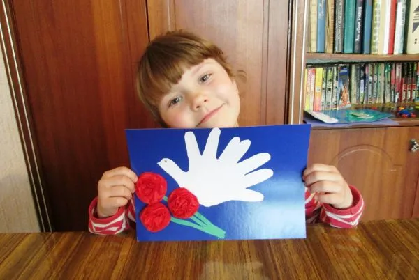 Девочка держит открытку с гвоздиками и голубем-ладошками