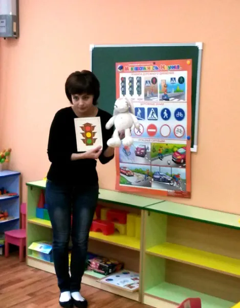 Педагог держит в руках игрушку и картинку с изображением светофора