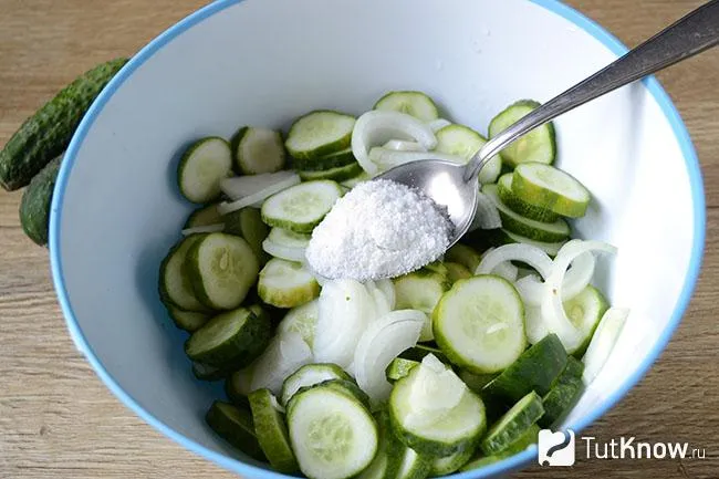 Ложка соли над миской с огурцами и луком